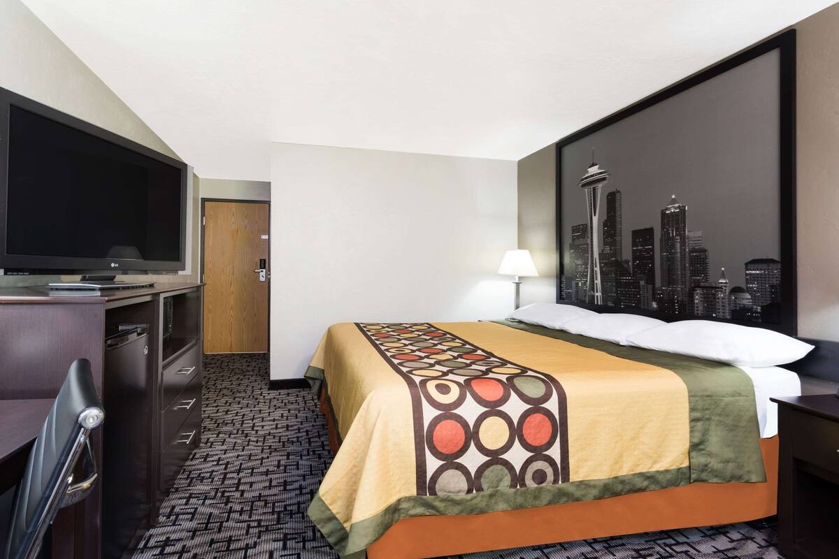 Ein Hotelzimmer mit Bett, Schreibtisch mit Fernseher, Blick auf die Stadt und einem gemusterten Teppich.