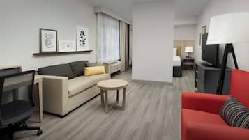 Una habitación de hotel moderna con sofá, un sillón rojo, una mesa redonda, televisor y obras de arte en la pared.