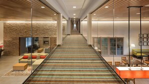 A modern hotel lobby with a long corridor, seating areas, and a fireplace.