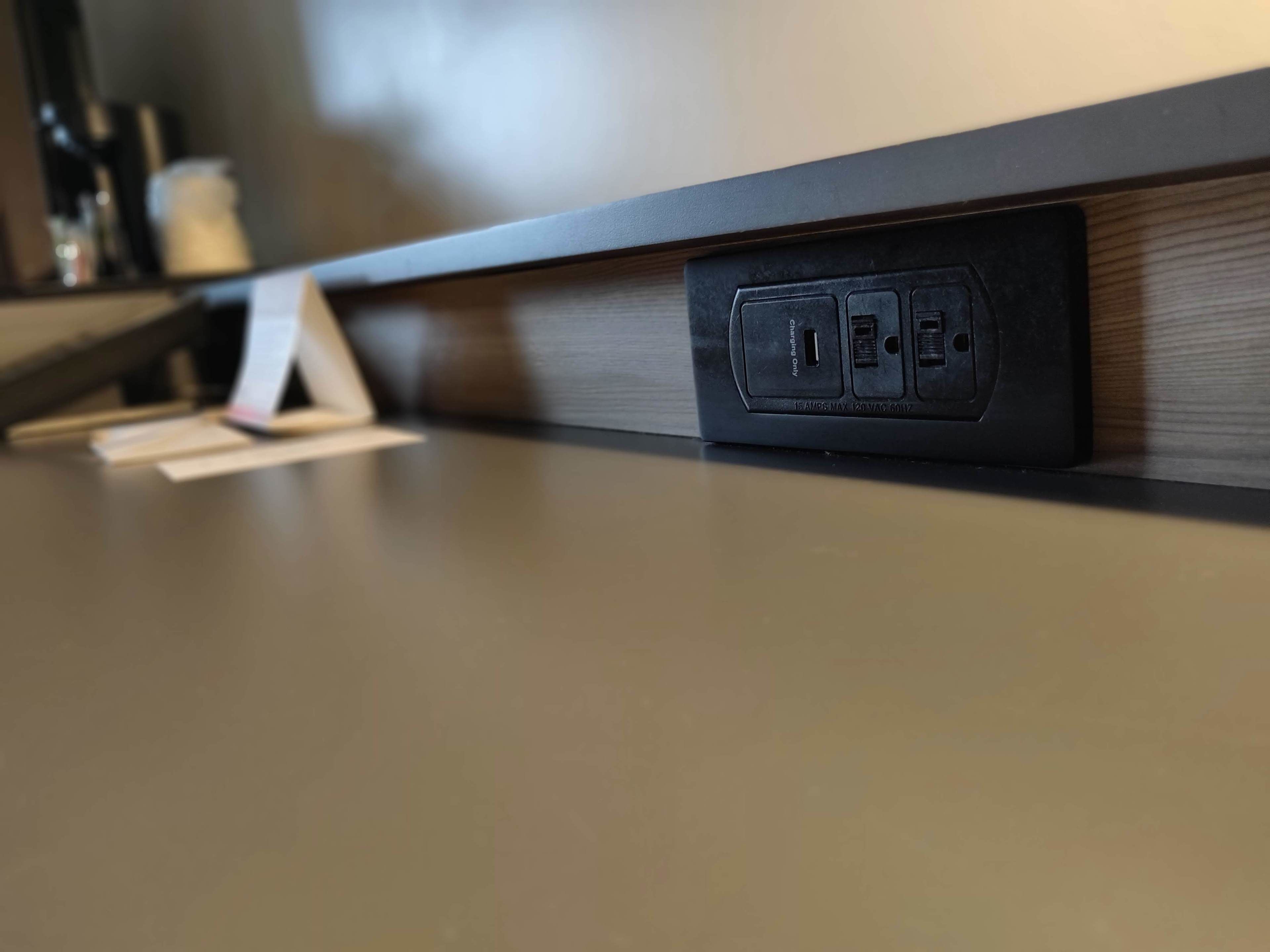 Primer plano de una toma de corriente con tapa negra, un puerto USB y una etiqueta que indica que es una toma de 15A 125V CA.