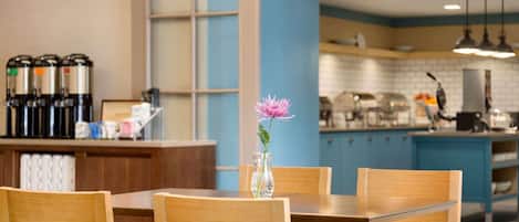 A modern kitchen with wooden chairs, a vase with a flower, and coffee machines.