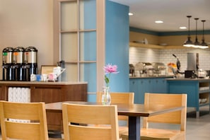 A modern kitchen with wooden chairs, a vase with a flower, and coffee machines.