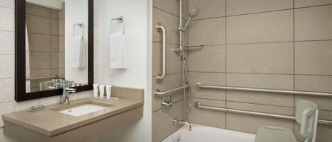 A modern bathroom with a large mirror, a sink, a shower with grab bars, and a wheelchair-accessible seat in the tub.