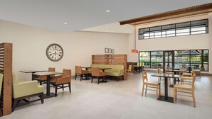 A spacious dining area with multiple tables and chairs, a clock on the wall, and large windows providing natural light.