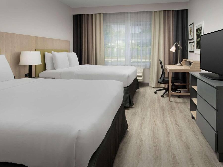 A hotel room with two beds, a desk, a chair, a television, and a window with curtains.