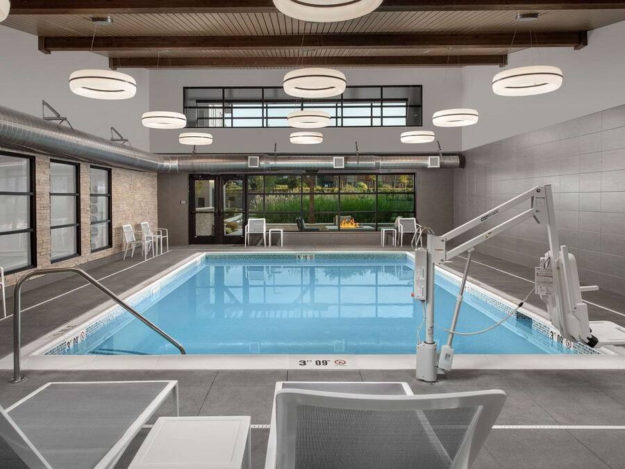 Una piscina interior moderna con agua cristalina, rodeada de sillones de descanso y vistas a zonas verdes.