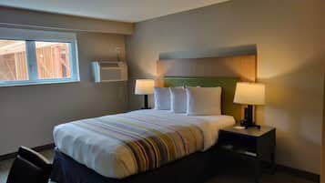 Hotelkamer met een groot bed, twee bedlampen, een raam met een airconditioner en uitzicht op een bouwplaats.