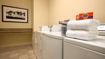 A laundry area with a Tide detergent box, a folded white towel, and a framed picture on the wall.