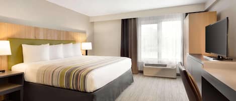 A hotel room with a large bed, a desk with a TV, a desk lamp, and a window with curtains.