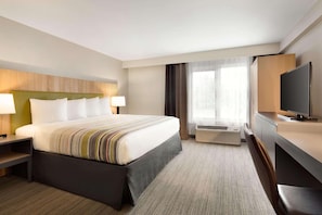 A hotel room with a large bed, a desk with a TV, a desk lamp, and a window with curtains.