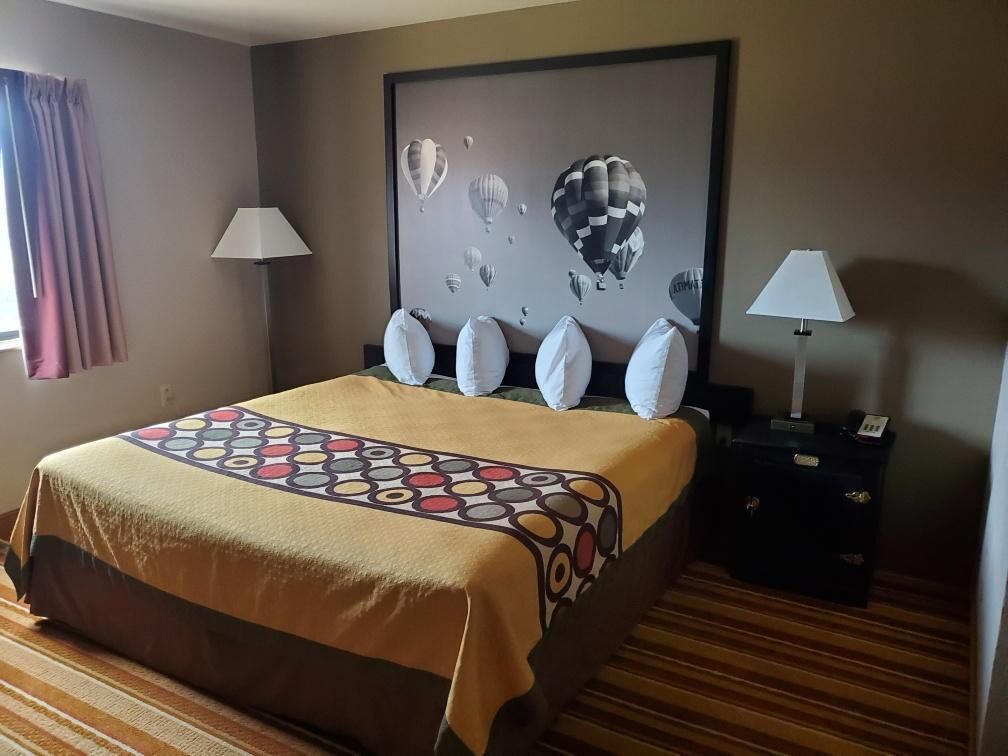 A hotel room with a bed, a nightstand, a lamp, and a wall art piece.