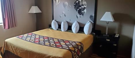 A hotel room with a bed, a nightstand, a lamp, and a wall art piece.