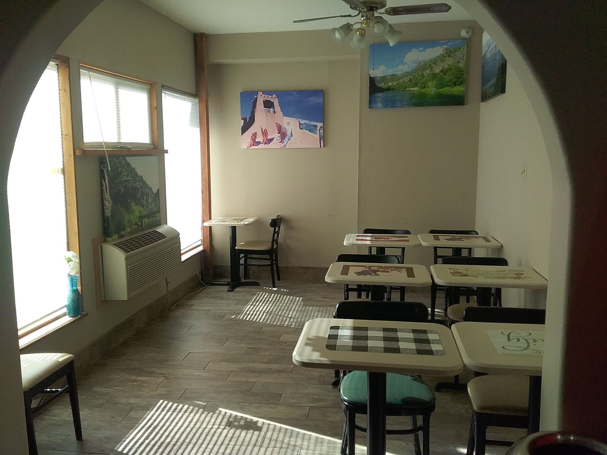 A classroom with tables and chairs, a ceiling fan, and a painting on the wall.