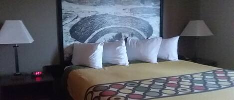 A hotel room with a bed, two bedside lamps, a nightstand, and a large framed picture on the wall.
