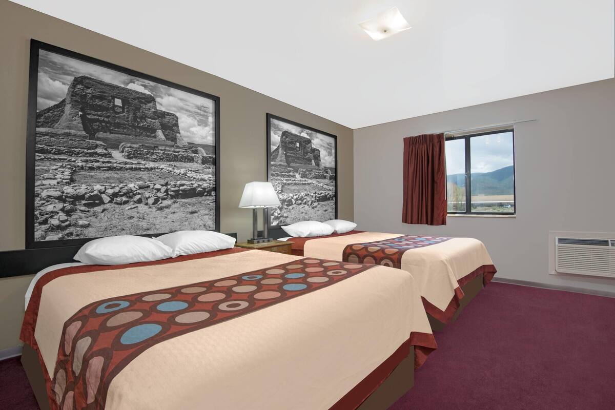 Een hotelkamer met twee bedden, een groot raam met uitzicht en twee ingelijste foto’s aan de muur.