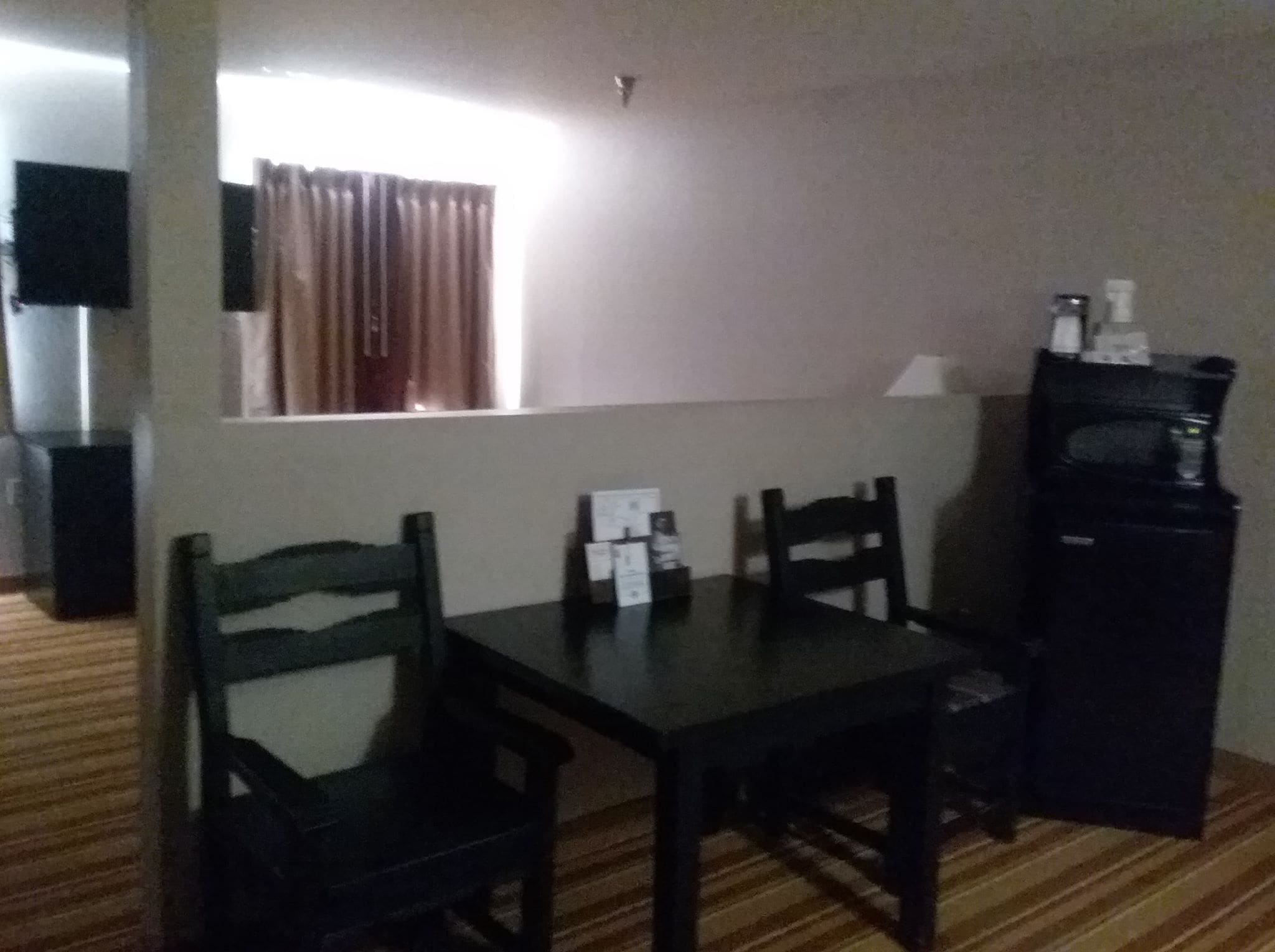 Una habitació petita amb un terra de fusta, una taula amb dues cadires, una televisió a l'esquerra i un frigorífic a la dreta.