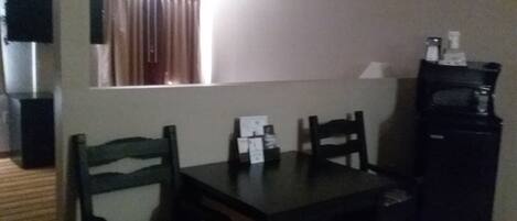 A small room with a wooden floor, a table with two chairs, a television on the left, and a refrigerator on the right.