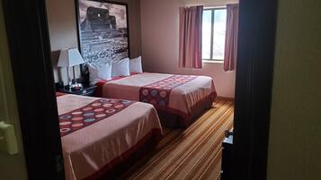 A hotel room with two beds, a large framed picture on the wall, a window with curtains, and a striped carpet.