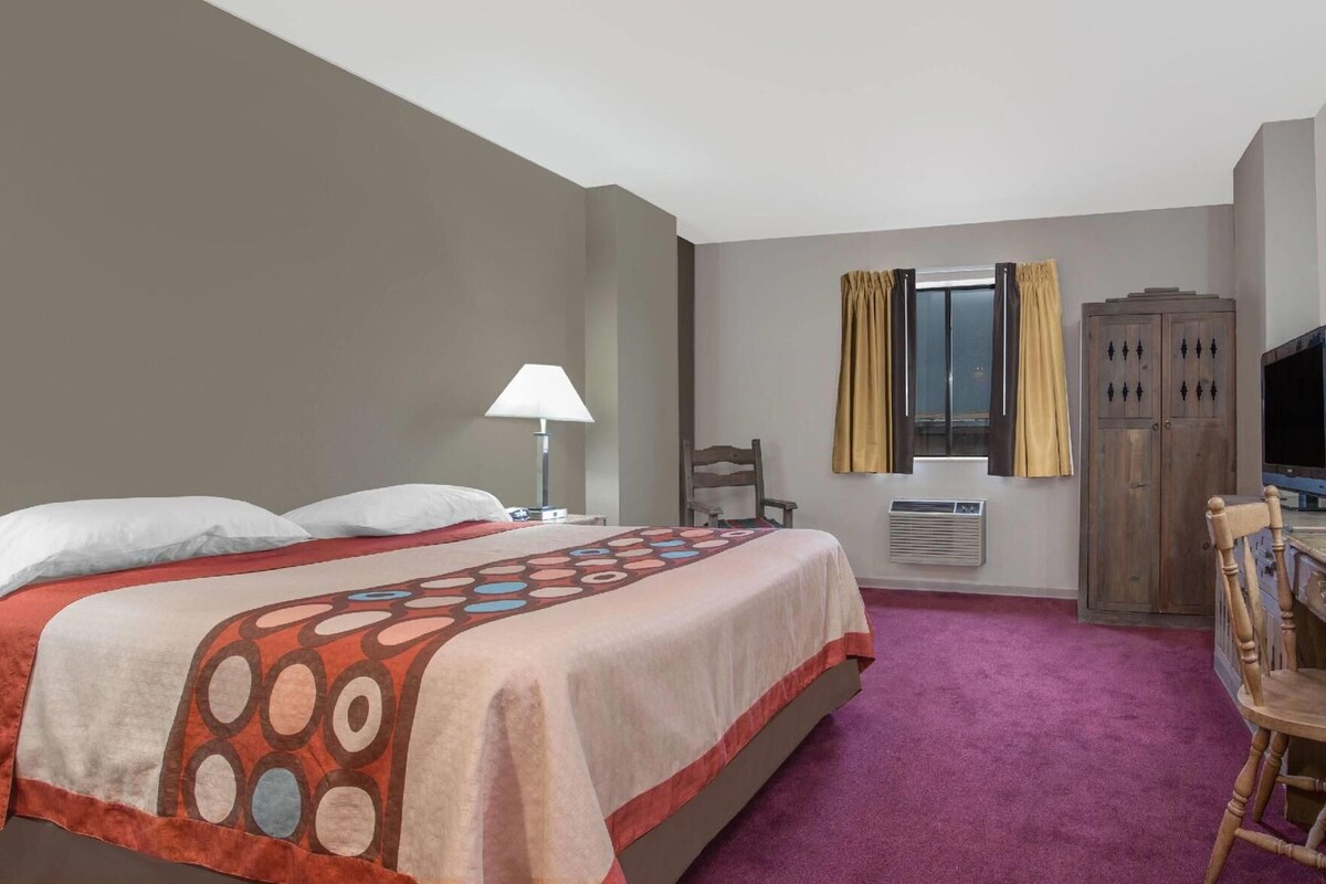 A hotel room with a bed, a desk, a chair, a TV, a wardrobe, and a window with curtains.