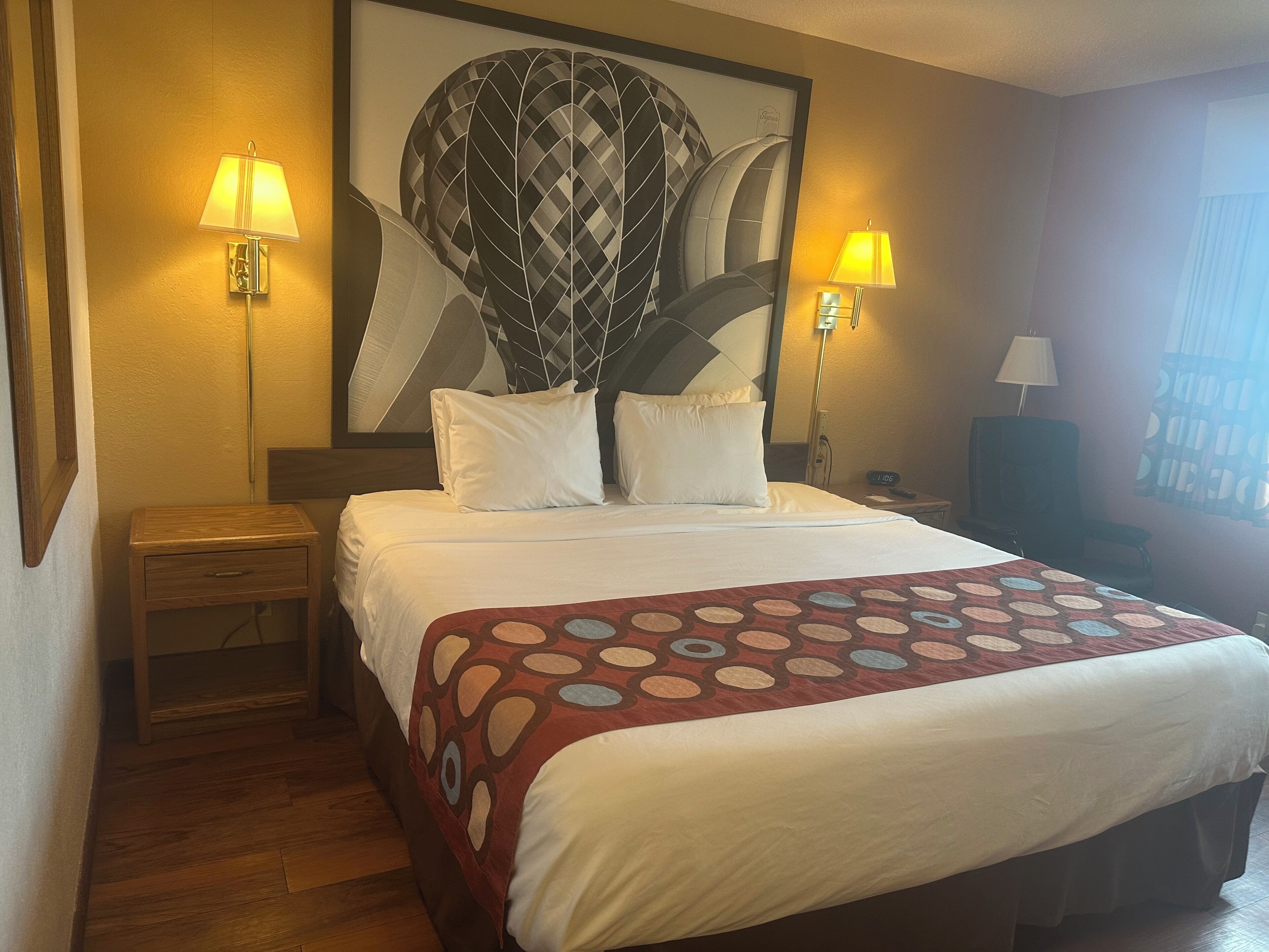 A hotel room with a large bed, two bedside lamps, a nightstand, a wooden floor, and a wall-mounted artwork.