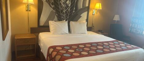 A hotel room with a large bed, two bedside lamps, a nightstand, a wooden floor, and a wall-mounted artwork.