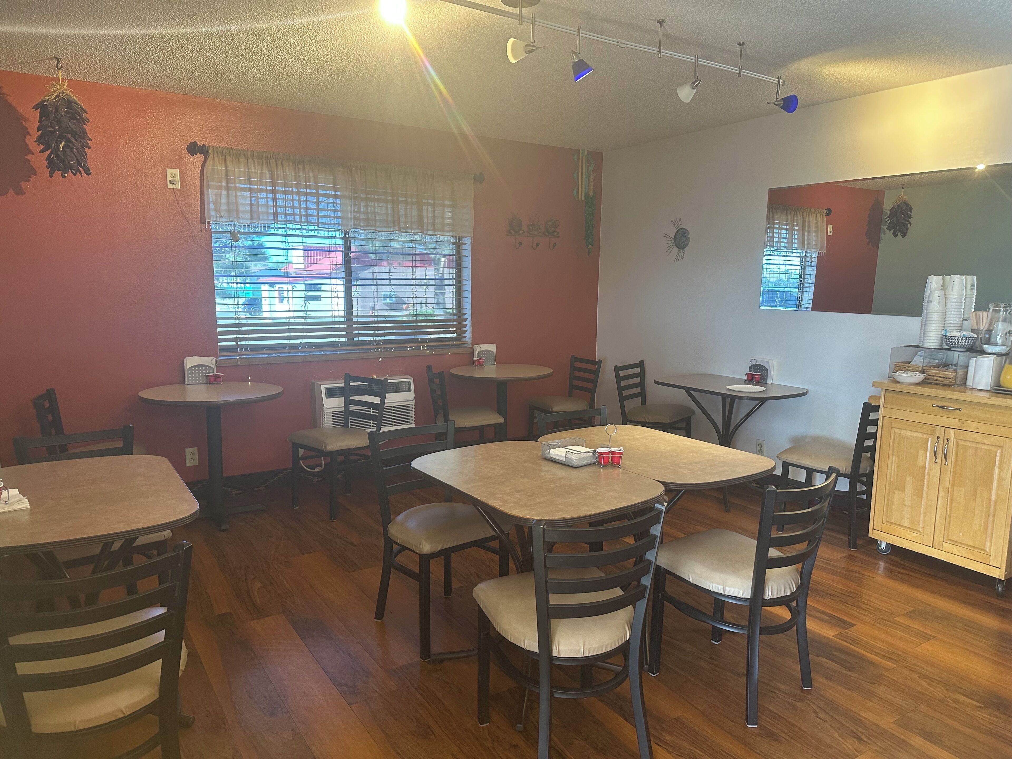 A restaurant interior with multiple tables and chairs, a window with blinds, and a counter with various items.