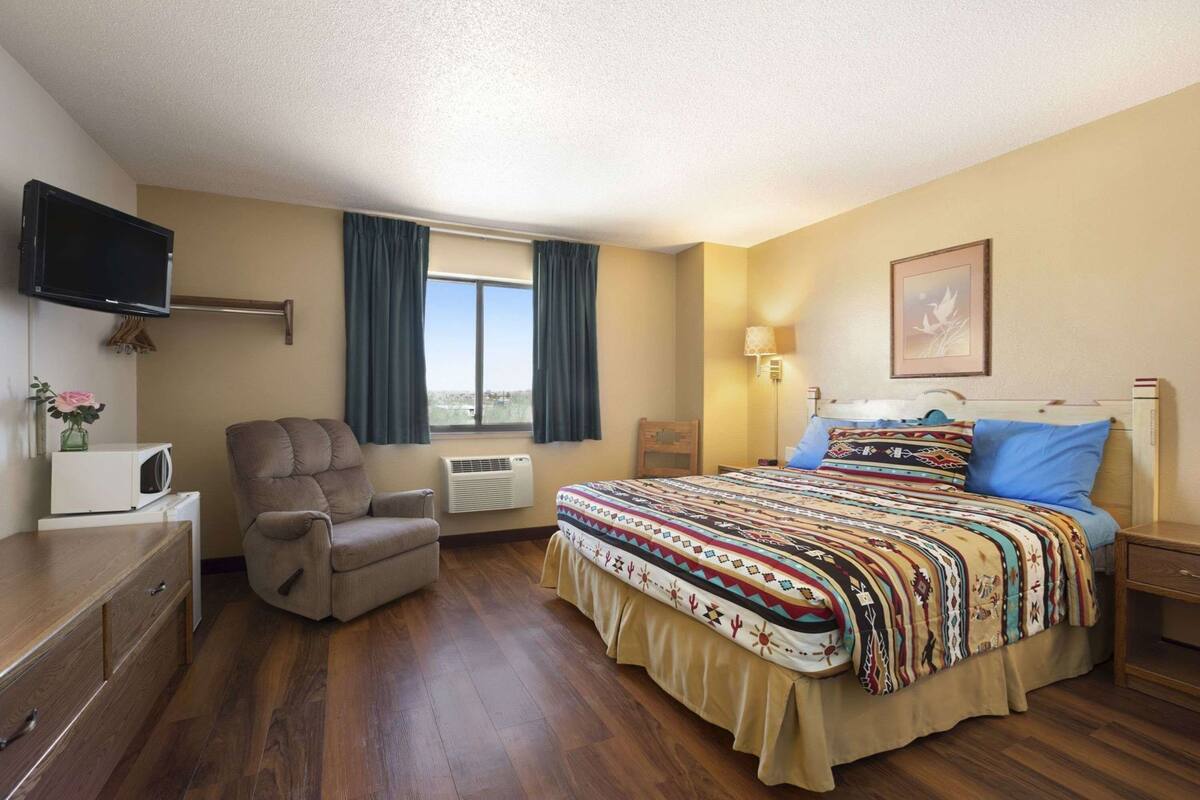 Une chambre d’hôtel avec un lit, une chaise, un bureau, une télévision et une fenêtre avec des rideaux.