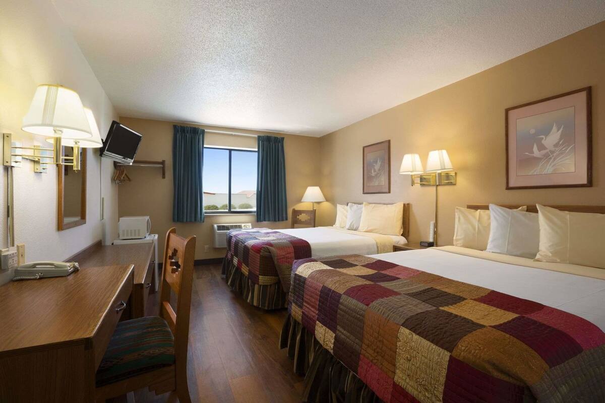 Une chambre d’hôtel avec deux lits, un bureau, une chaise, une télévision et une fenêtre avec des rideaux.
