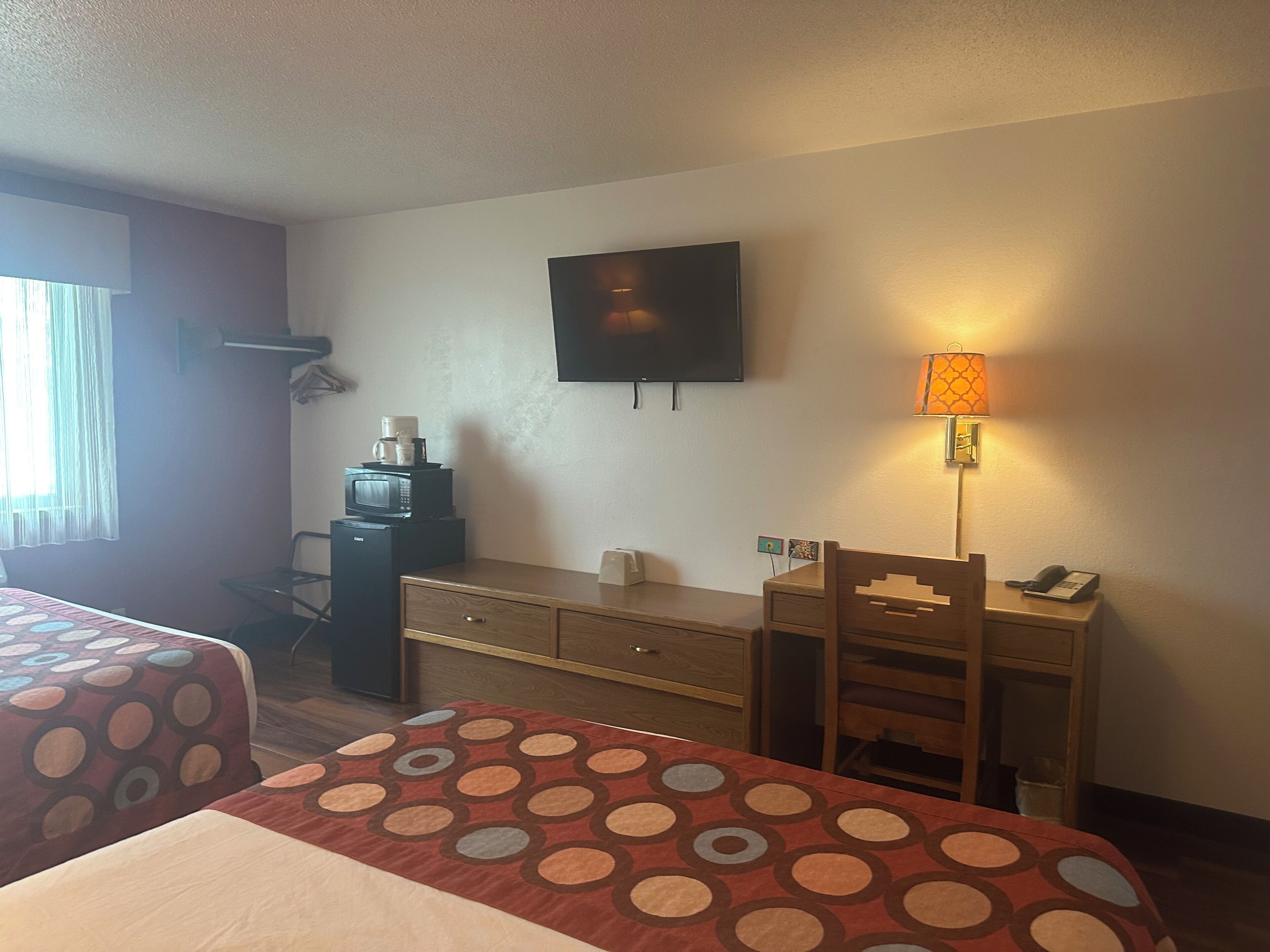 A hotel room with two beds, a desk, a television, a lamp, and a microwave.