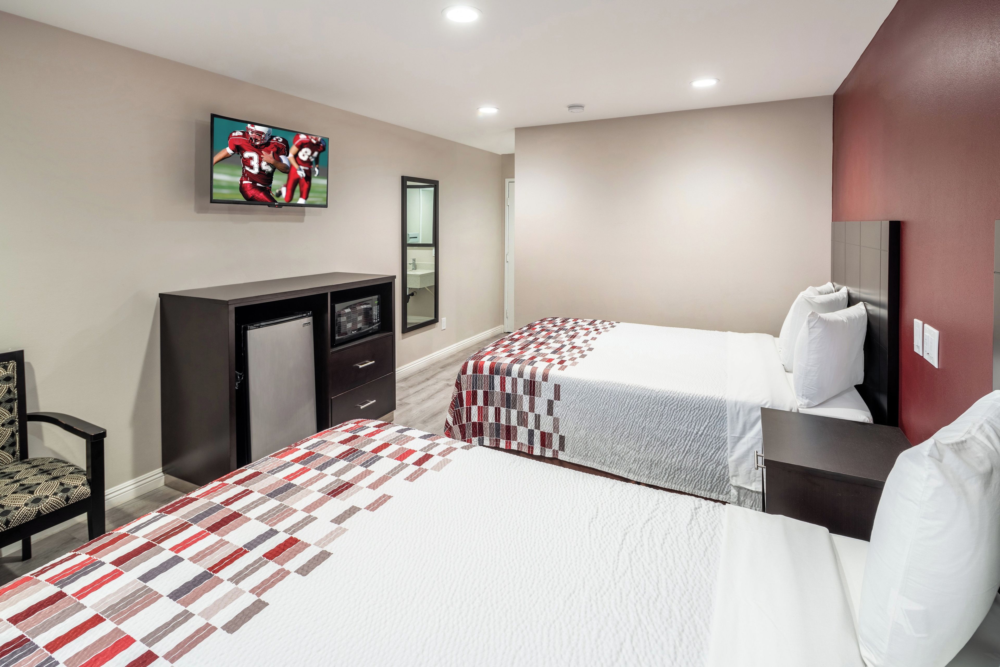 Une chambre d’hôtel avec deux lits, une télévision, un bureau, une chaise et un miroir.