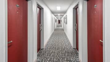 Un pasillo de hotel con puertas rojas, paredes blancas y alfombra estampada.