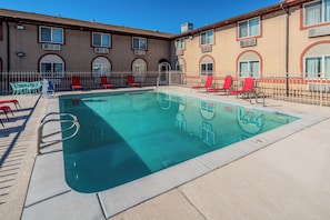 A swimming pool with a metal ladder, surrounded by a fence, and red chairs. - Red Roof Inn St George, UT - Convention Center (St. George)