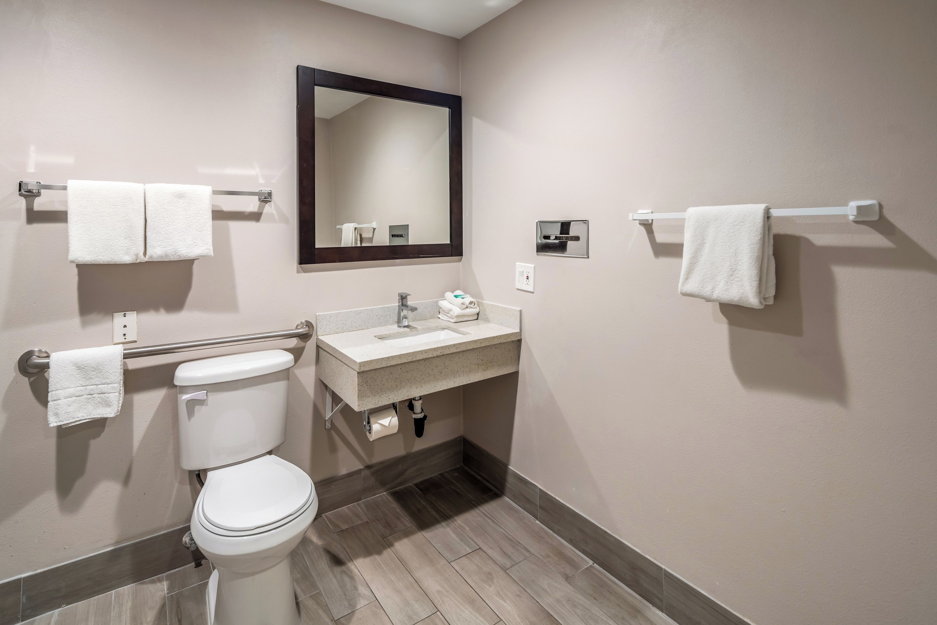Un baño con inodoro, lavamanos, espejo y toalleros.