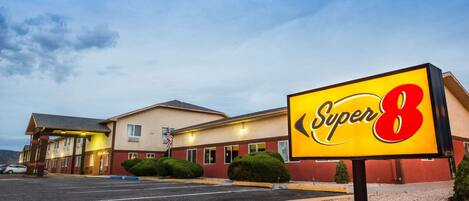 Un motel Super 8 con un letrero iluminado grande, un estacionamiento y un edificio de múltiples ventanas y techo plano.