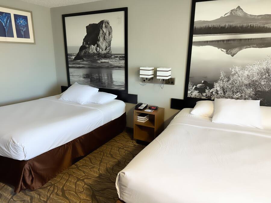 A hotel room with two beds, a nightstand, and artwork on the walls.
