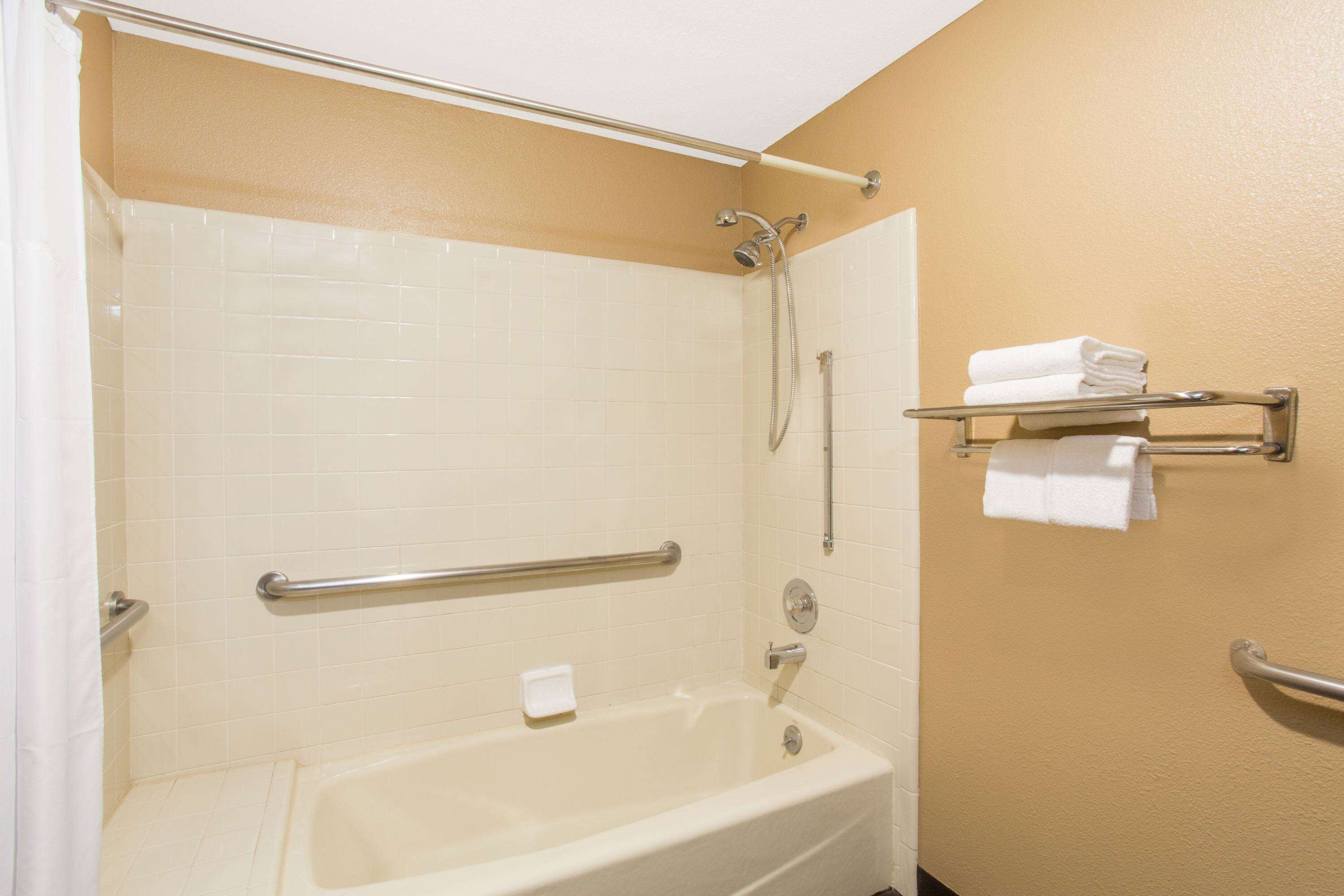 A bathroom with a bathtub, a shower, and a handrail.