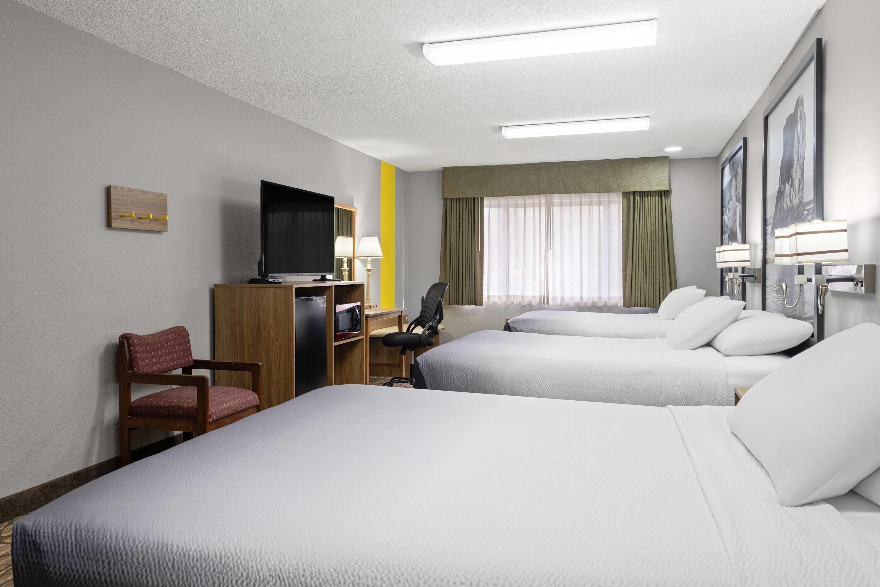 A hotel room with two beds, a desk with a TV, a chair, and a window with curtains.