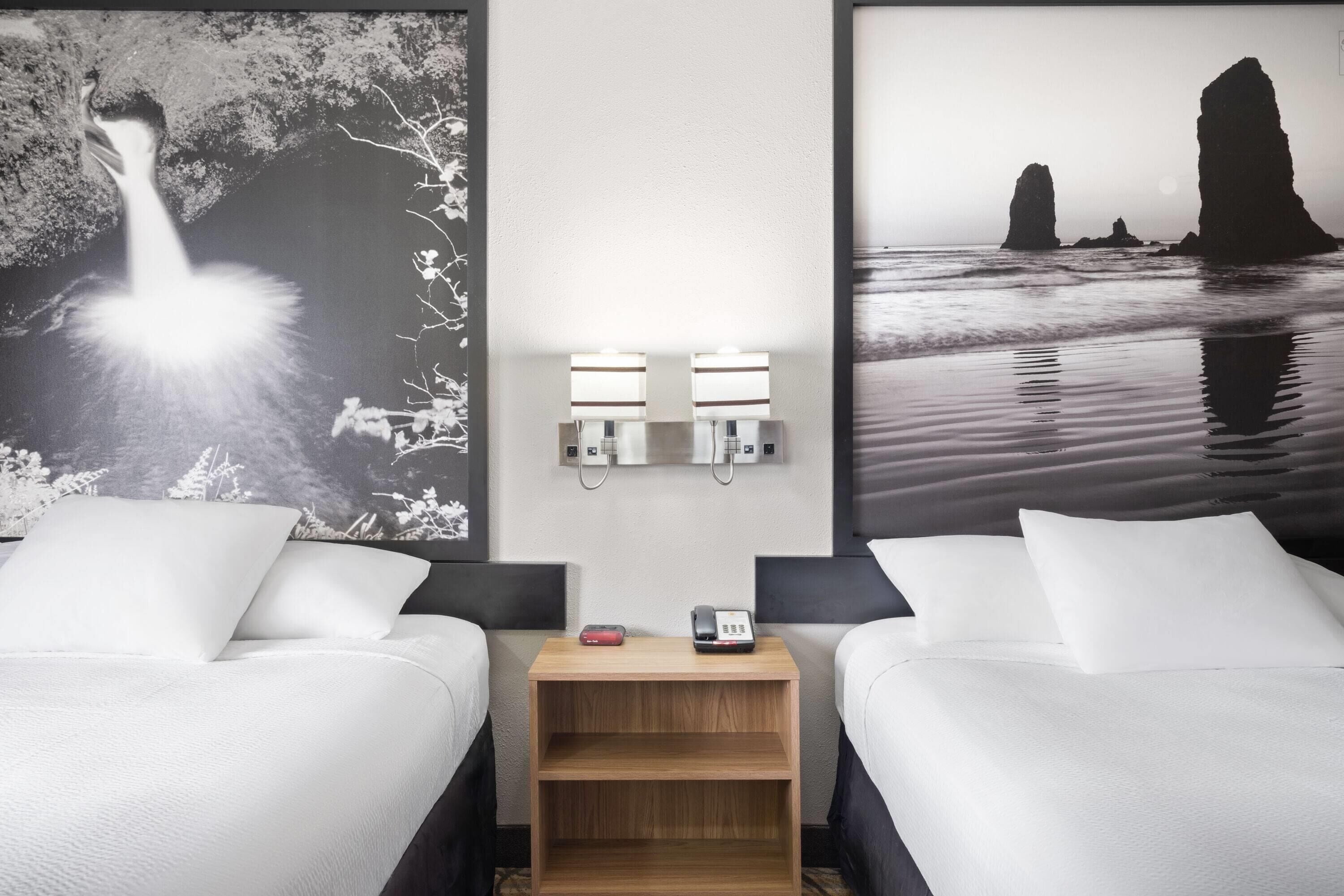 Quarto de hotel com duas camas, mesa de cabeceira com telefone e arte na parede retratando um pássaro e formações rochosas.