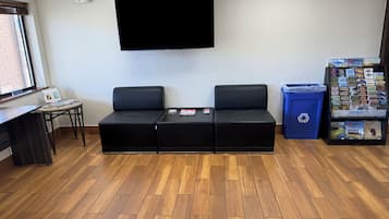 A room with a black sofa, a small table with a chair, a bulletin board, and a blue recycling bin.