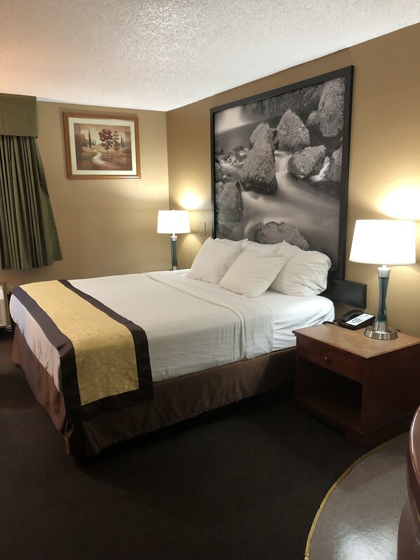 Habitación de hotel con una cama grande, dos lámparas de noche, una mesita de noche con un teléfono y un cuadro en la pared.