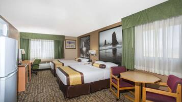 A hotel room with two beds, a desk, a chair, a small table, and a refrigerator.