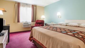 A hotel room with a large bed, a desk with a lamp, a chair, and a TV.