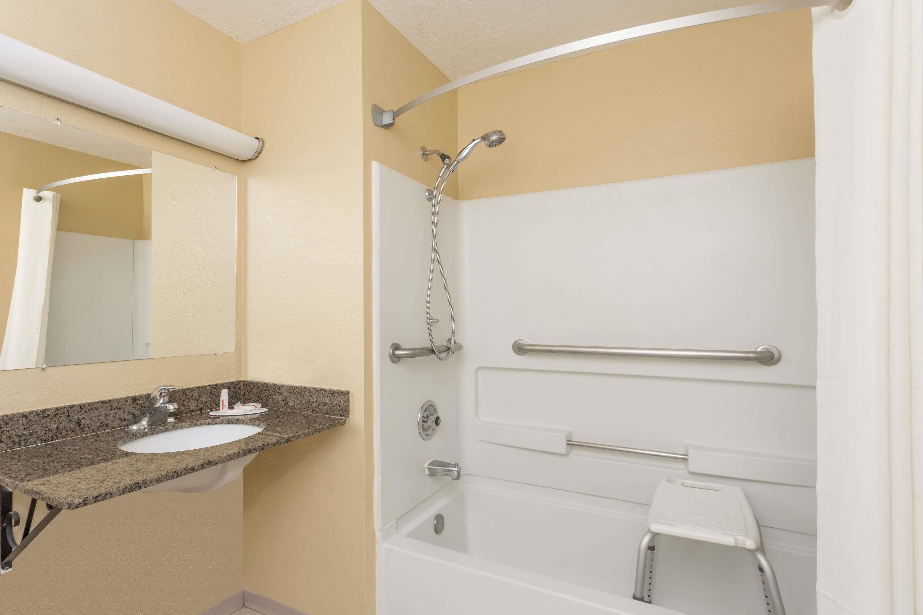 A bathroom with a sink, mirror, shower, and grab bars.