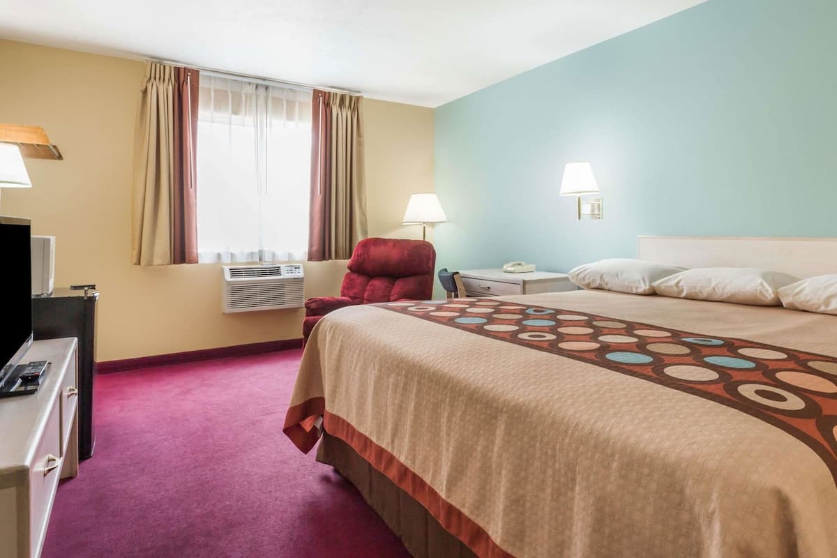 A hotel room with a bed, a desk, a chair, a TV, and a window with curtains.