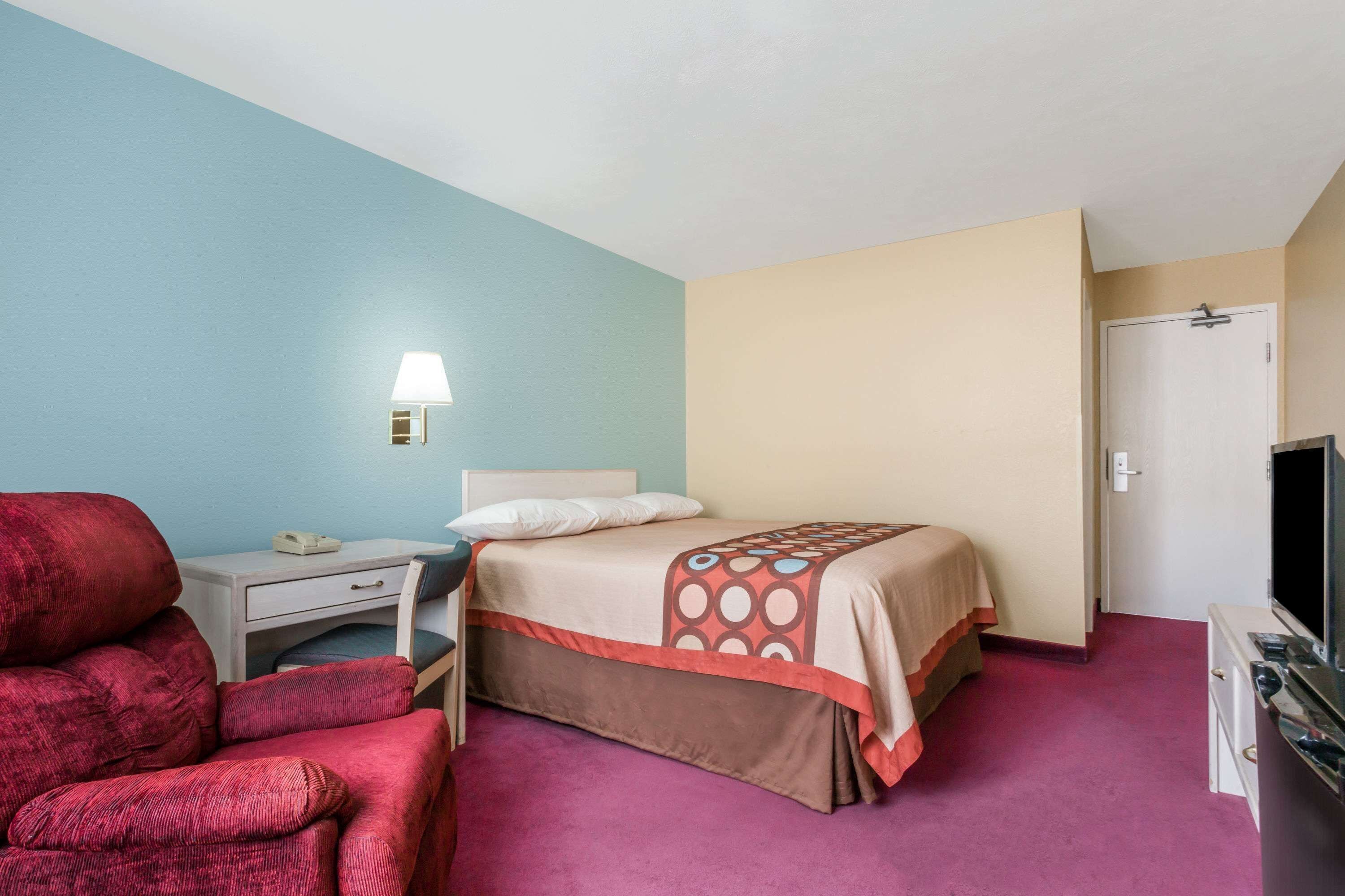 Una habitación de hotel con una cama, un escritorio, una silla, un televisor y una puerta.
