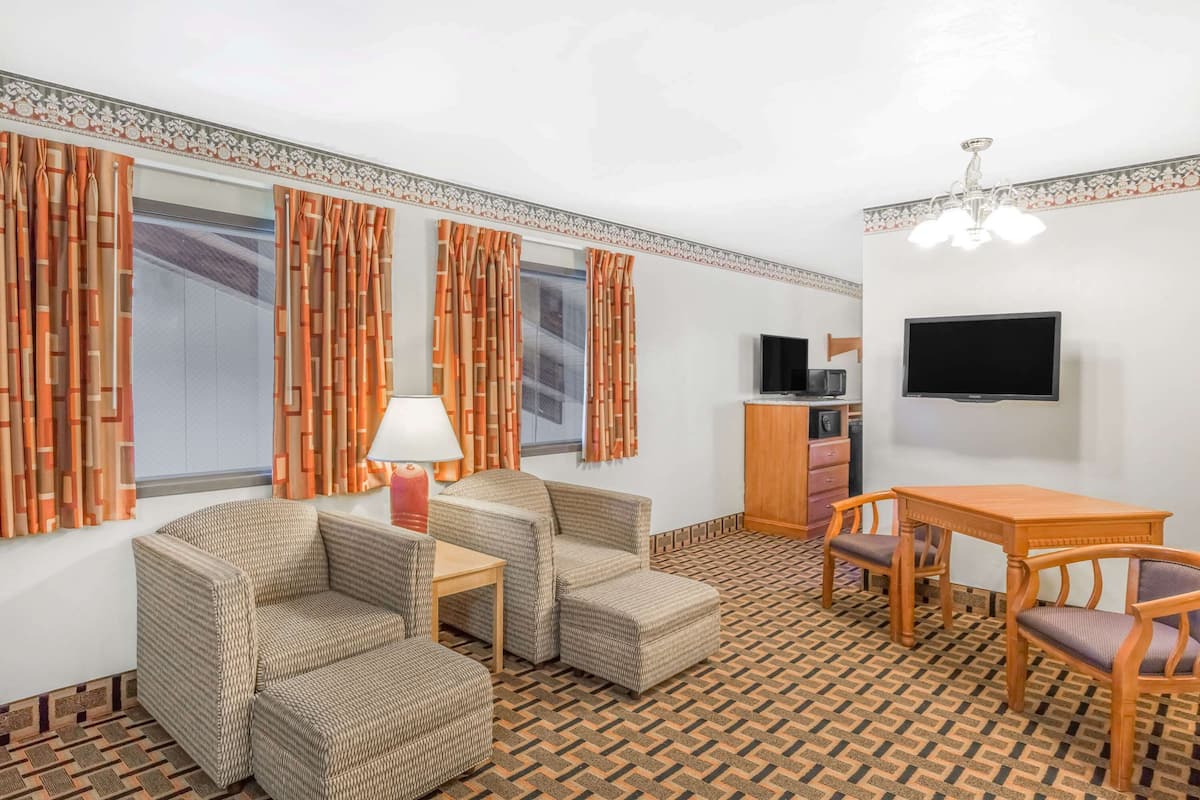 Een kamer met een bank, twee fauteuils, een kleine tafel, een televisie en een kamer met een patroon vloer.