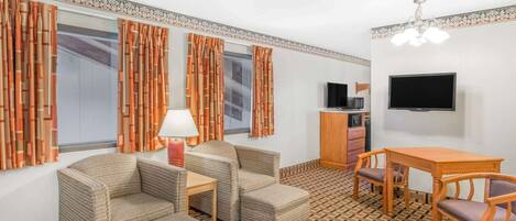 A room with a sofa, two armchairs, a small table, a TV, and a patterned floor.