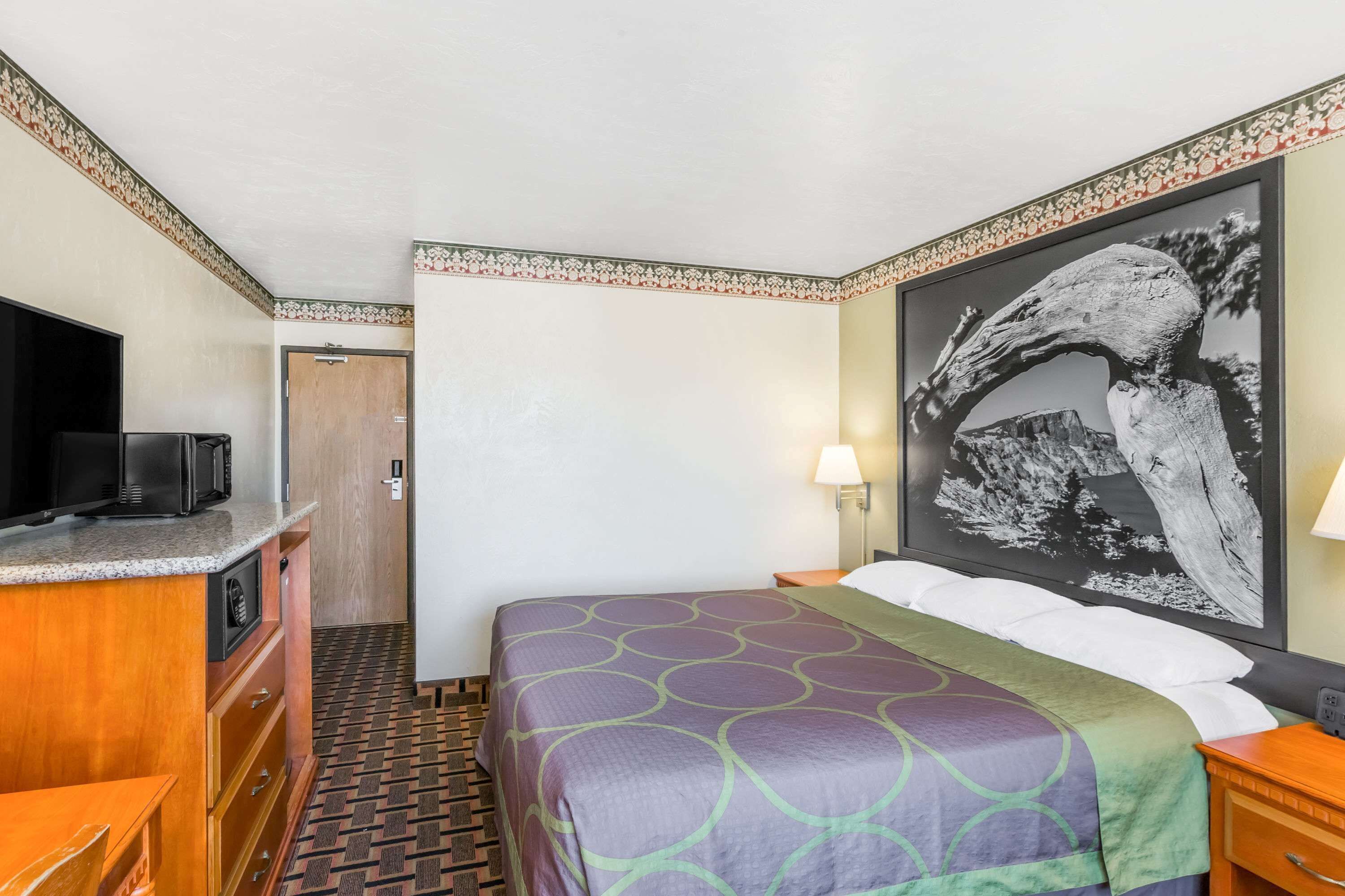 A hotel room with a bed, a TV, a desk, and a door.