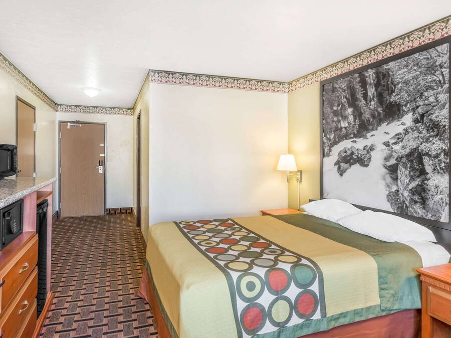 A hotel room with a bed, a desk, a television, and a painting on the wall.