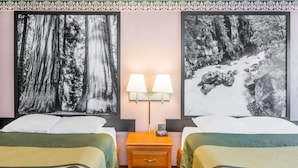 Habitación de hotel con dos camas, una mesita de noche con lámparas y dos grandes cuadros con motivos forestales.